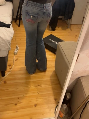Blå bootcut jeans med slitningar - Bootcut jeans i ljusblå denim med slitna detaljer och hål på knäna. Bakfickorna har dekorativa sömmar i rosa. Klassisk femficksmodell med knapp och dragkedja. Perfekta för en avslappnad och trendig look.