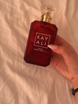Kayali Lovefest Burning Cherry parfym - Nästintill helt oanvänd Kayali Lovefest Burning Cherry som jag fått i present den luktar väldigt gott men personlig tycker jag inte om körsbär. Det är en parfym i en lyxig, mörkröd glasflaska med guld- och kristalldetaljer på korken. Flaskan har en modern, kantig form och tydlig vit logga framtill. Doften är känd för sina söta och fruktiga körsbärstoner.