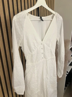 Vit långklänning från h&m - Vit långklänning med diskret prickigt mönster, v-ringning och knappar framtill. Klänningen har långa ärmar och markerad midja för en smickrande siluett. Perfekt för sommarens alla tillfällen.  Skriv om ni vill ha bild på 🫶🏼🫶🏼