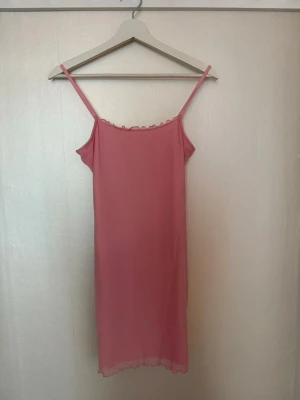 Rosa sommarklänning med tunna axelband - Sött stretchig rosa sommarklänning med tunna axelband och volangkant upptill och nertill. Lätt och luftigt material, perfekt för att stranden. Enkel och stilren design utan mönster.