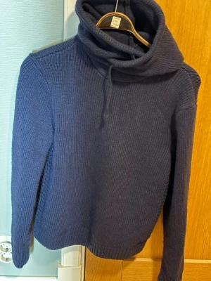 Mörkblå stickad hoodie Pier One - Mysig mörkblå stickad tröja från Pier One med hög krage och stor luva där back, goa mönster på tröjan. 
