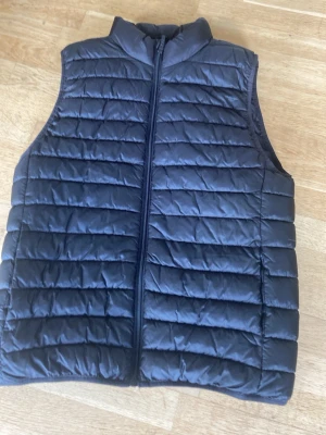 Svart quiltad väst - Stilren svart väst med quiltat mönster och dragkedja framtill. Den är lätt vadderad.