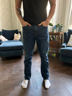 Mörkblå raka jeans herr - Snygga mörkblå jeans med rak passform och klassisk femficksdesign. Jeansen har normal midja och är tillverkade i ett robust denimtyg. Perfekta för en avslappnad och stilren look. Från NN07!! Dem är i strl 32/32