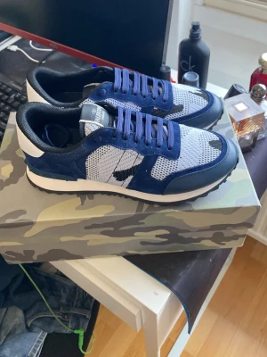 Valentino rockrunners - Snygga sneakers från Valentino Garavani i blått och vitt med mesh och mockadetaljer. Skorna har vita och svarta inslag, blå snören och coola nitar på hälen. Perfekt för dig som vill ha något unikt och trendigt till din outfit.