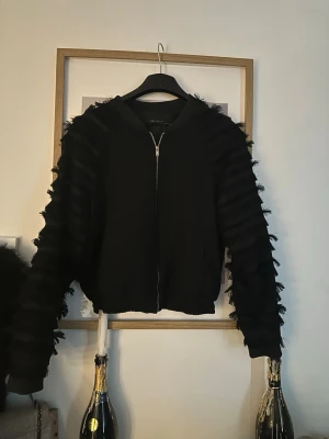 Bomberjacka med fjädrar  - Svart bomberjacka med fjäder armar, och guld kedja, använd 2 gånger i fint skick❤️