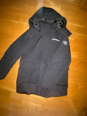  Calvin Klein jacka – Stilren & Varm - Säljer en snygg och stilren svart vinterjacka från Calvin Klein. Jackan har huva och en modern design som passar perfekt både till vardag och finare tillfällen.  Den är varm, bekväm och har en minimalistisk look med diskret Calvin Klein logga på bröstet samt CK märke på ärmen.  Perfekt för höst och vinter 🌨️  Mått: • Längd: 66 cm • Bredd: 49 cm