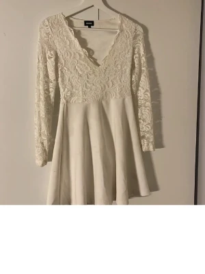 Vit spetsklänning från Bubbleroom - Supersöt vit klänning från Bubbleroom med långärmade spetsdetaljer och v-ringad urringning. Överdelen är helt i spets och kjolen är slät och utsvängd. Perfekt för dig som tar studenten❤️missfärgad vid spetsen och små fläckar som ni kan se på bild 3 och 4❤️tips att bleka det i klorin för att ta bort 