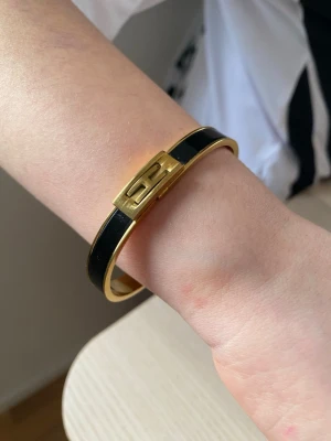 Svart och guld H armband - Snyggt armband från H i svart och guld. Armbandet har en elegant, stilren design med svart emalj och guldfärgad metall samt det klassiska H-spännet framtill. Perfekt accessoar för att lyfta din outfit.