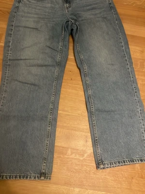 Blåa raka jeans från Kappahl - Säljer ett par blåa raka jeans från Kappahl med klassisk femficksmodell och hög midja. Jeansen har en tvättad look och bredare ben, perfekta för en avslappnad stil. Materialet är denim i bomull. Snygga att matcha med sneakers eller boots!
