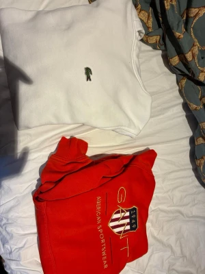 Röd hoodie från GANT - Säljer en röd hoodie från GANT med broderad logga och texten 'American Sportswear' framtill. Hoodien har klassisk huva och ribbade muddar vid ärmslut och nederkant. Perfekt för en sportig och avslappnad stil. Vi kan snacka mer om prisert senare o storlekarna är ” den röda är 134/140 den vita är 164cm” 