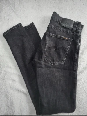 Svarta Nudie Jeans – Tidlös modell, perfekt passform 🖤 - Säljer ett par svarta jeans från Nudie Jeans i fint skick. Klassisk modell med perfekt passform som sitter snyggt och funkar till allt – både vardag och fest. Djup svart färg och stilren design gör dem till ett måste i garderoben. Bekväma, kvalitativ denim och lätta att matcha. Passa på att fynda ett par tidlösa jeans till bättre pris än i butik! 💬skriv frågor och om ni vill ha fler bilder! 🚛fraktar direkt!