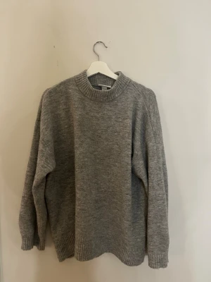Grå stickad tröja i ullmix - Mysig grå stickad tröja med rund hals och ribbade muddar vid ärmslut och nederkant. 