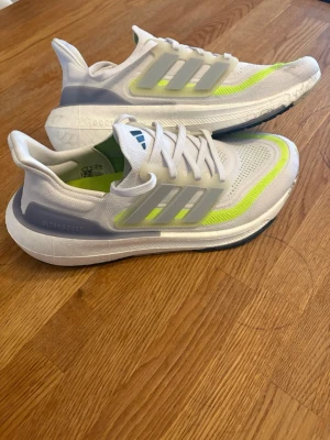 Adidas Ultraboost vita sneakers - Fräscha Adidas Ultraboost sneakers i vitt med grå och neongula detaljer. Ovandelen är i mesh för bra andningsförmåga och sulan är tjock och stötdämpande. Klassiska tre ränder på sidan och snörning framtill. Perfekta för dig som gillar sportig stil.