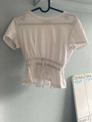 Vit croppad topp med snörning från Zara - Söt vit croppad topp med korta ärmar och snörning i midjan som ger en snygg passform. har tre små hål men de snyns knappt, därav priset. 
