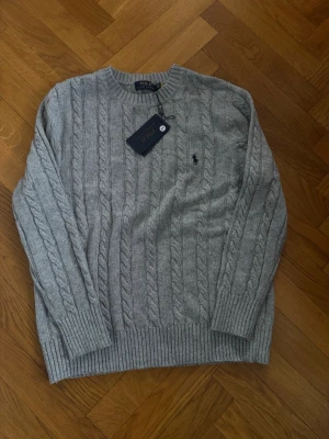 Grå kabelstickad tröja Polo Ralph Lauren - Snygg grå kabelstickad tröja från Polo Ralph Lauren. Aldrig använd! Passar bäst M/L