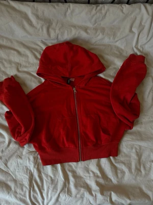 Röd zip hoodie med huva - Snygg röd hoodie med dragkedja framtill och stor huva. Modellen är croppad med bred mudd i midjan och har två fickor framtill. Perfekt för en avslappnad och trendig look. Materialet känns mjukt och bekvämt, troligen bomullsblandning.