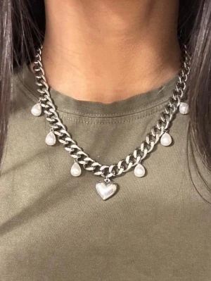 Silvrigt halsband med hjärthänge och droppformade . - https://vm.tiktok.com/ZNRDKN37d/   Presentask ingår. Det finns möjlighet att köpa utan preesentask till ett lägre pris (se en annan annons på min sida).  Matchande örhängen finns i en separat annons. Finns även i guldpläterad variant.  Material: 18K guldplätering på rostfritt stål Bredd: 9 mm Längd: 38-43cm Nickelfria och handgjorda.
