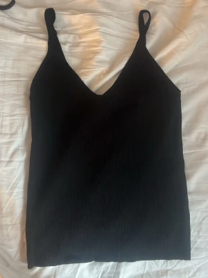  ribbade linne-toppar  - Säljer två stilrena ribbade linne-toppar med smala axelband, en i svart och en i klarblå färg. Båda har v-ringad hals och är tillverkade i mjukt stretchigt material som sitter snyggt på kroppen. Perfekta att matcha med jeans eller kjol.