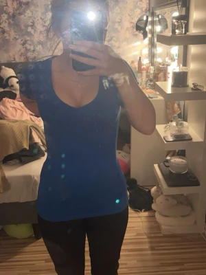 Blå tight v-ringad topp - Snygg blå topp med v-ringning och korta ärmar. Modellen är tight och figurnära, perfekt för dig som gillar en enkel men stilren look. Passar till både jeans och kjol. Materialet känns mjukt och stretchigt.