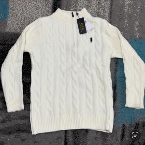 Vit Zip-Knit Polo Ralph Lauren - Vit Zip-Knit från Polo Ralph Lauren med halv dragkedja vid halsen och klassisk broderad logga på bröstet. Tröjan har ribbade muddar och är perfekt för en stilren look. TVEKA INTE ATT SKICKA EN BUD:)
