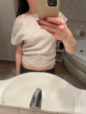 Beige offshoulder topp - Trendig ljusgrå offshoulder topp i mjukt material. Toppen har en croppad passform och korta ärmar, perfekt för en avslappnad och modern look. Enkel att matcha med både jeans och kjol.