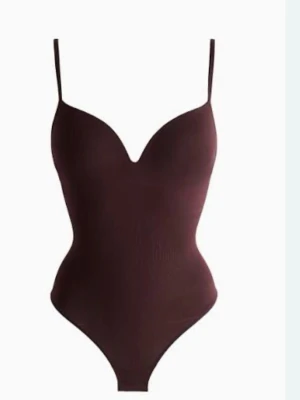 Mörkbrun body med smala axelband - Snygg vinröd body med smala axelband och v-ringning. Figurnära passform som framhäver siluetten. Perfekt att styla med jeans eller kjol för en trendig look.