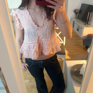 Ljusrosa/ aprikos volangblus med knappar - Supersöt ljusrosa/ aprikos färgad blus med volanger och knappar framtill. Korta ärmar med volangdetaljer och luftig passform. Så snygg nu till när våren är påväg💗💗 