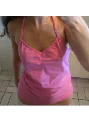 Rosa topp - Säljer en rosa halterneck-linnetopp från Marwin. Toppen har en snygg v-ringning och smala axelband som knyts i nacken. Perfekt för varma dagar och enkel att matcha med jeans eller kjol. Passar s och xs också 