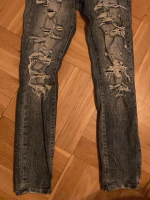 Blå slitna ripped jeans Jordan Craig Legency Edition storlek 12 år - Säljer ett par Jordan Craig blå jeans med designade slitningar framtill. Jeansen har fem fickor, smal passform och en cool, tvättad look. Perfekta för dig som gillar en edgy och trendig stil. Storlek junior 12 år.