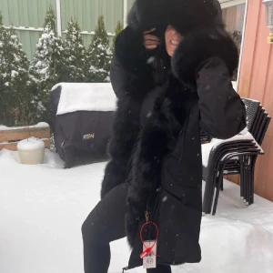 Svart parkas med stor äktapäls - Snygg svart parkas med stor, fluffig äkta päls runt huva och öppning. Jackan har dragsko i midjan, fickor på sidorna och stängs med dragkedja. Perfekt för kalla vinterdagar och ger en lyxig känsla till din outfit.