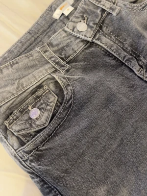 Gråa jeans med bakfickor - Säljer ett par gråa  jeans med fina bakfickor och silverfärgade knappar både fram och bak. Väldigt snygga och formar. Ger verkligen Y2K vibe!! Dem är storlek 164 som motsvarar ungefär xs/s