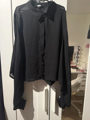 Svart skjorta med långa ärmar - Säljer en svart skjorta från Gina Tricot med klassisk krage och knappar framtill. Skjortan har långa, lösa ärmar och är tillverkad i ett tunt, lätt material som ger ett snyggt fall. Perfekt för dig som gillar en stilren och enkel look.