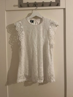 Vit spetsblus  - Säljer en superfin vit blus från Pieces i spets med detaljerade volangkanter vid ärmarna. Blusen är ärmlös och har rund halsringning samt knapp i nacken. 