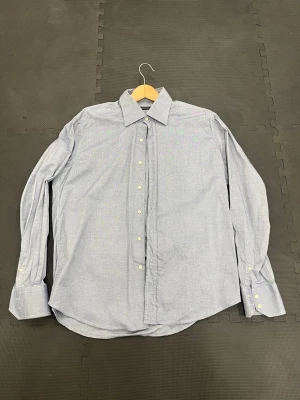 Valentino skjorta  - Klassisk valentino ljusblå skjorta i bomull med lång ärm och vita knappar framtill. Skjortan har en normal passform och stilren krage, perfekt för en clean och enkel look. Passar till både jeans och chinos.