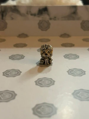 Pandora lejonberlock i silver 925 - Unik Pandora berlock i form av ett lejon, tillverkad i silverfärgat metall. Detaljerad design med man och tassar, samt en liten brittisk flagga undertill. Perfekt för att ge din armbandslook en personlig touch.