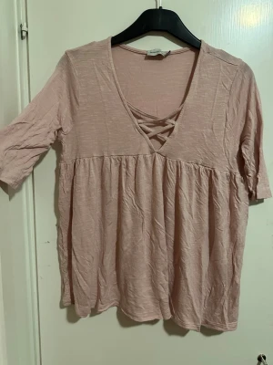 Ljusrosa topp från Angelology - Supersöt ljusrosa topp från Angelology med v-ringning och snygg snörningsdetalj framtill. Toppen har halvlånga ärmar och ett flowy fall under bysten. Perfekt att styla med jeans eller kjol för en chill look.