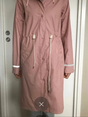 Rosa regnkappa stl XS Nyskick - Fin regnjacka/kappa rosa från Lindex. Stl XS, passar en small bra. Dragsko i midjan. Använd en gång, är i nyskick.  Nypris: 499:-