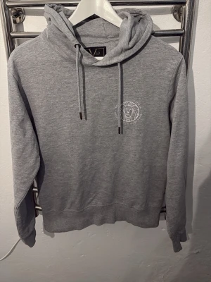 Grå hoodie från 169 med lejontryck - Snygg grå hoodie från 169 med dragsko i huvan och ett vitt lejontryck på bröstet. Tillverkad i mjukt bomullsmaterial och har ribbade muddar vid ärmar och nederkant. Perfekt för en avslappnad och trendig stil.