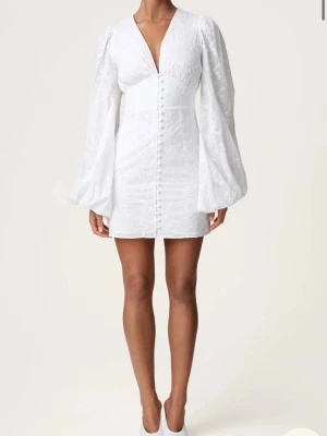 Adoore klänning - Superfin vit kort klänning med v-ringning, långa puffärmar och dekorativa knappar framtill. Klänningen har en figurnära passform och är perfekt för sommarens alla tillfällen. Tunt, lätt material med subtil struktur. Använd 1 gång.