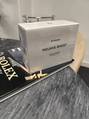 Byredo Mojave Ghost Eau de Parfum - Byredo Mojave Ghost Eau de Parfum i elegant vit förpackning med stilren svart text. Parfymen är känd för sin unika doftprofil och exklusiva känsla. Förpackningen är rektangulär och har en lyxig, minimalistisk design som passar perfekt för dig som gillar trendiga dofter.