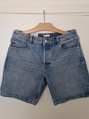 Blå denimshorts från Cubus - Klassiska blå denimshorts från Weekday med fem fickor och gylf med knapp och dragkedja. Modellen har en rak passform och är tillverkad i bomull. Perfekta för sommaren och enkla att matcha med allt. Jag vet inte om det är herr eller damshorts men passar ungefar till L (dam)