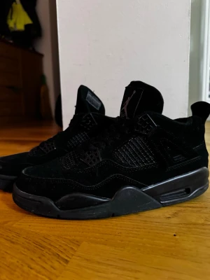 Svarta Air Jordan 4 Retro sneakers - För fler bilder skriv gärna och pris kan diskuteras. Säljer ett par helsvarta Air Jordan 4 Retro sneakers med ovandel i mocka och detaljer i mesh och plast. Skorna har den klassiska Jumpman-loggan på plösen och en kraftig sula med synlig Air-enhet. Perfekta för dig som gillar stilrena och ikoniska sneakers.