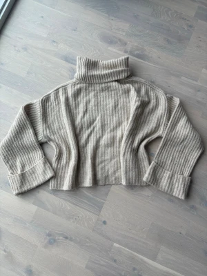 Beige polotröja från Gina Tricot - Stickad beige polotröja från Gina Tricot i ribbat material. Tröjan har breda ärmslut, croppad passform och hög polokrage. Perfekt för lager på lager och en chill look. Materialet känns mjukt och mysigt.