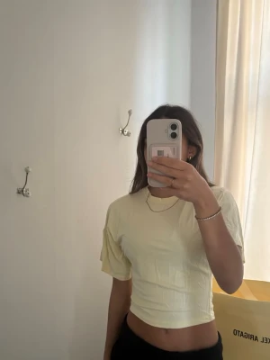 Ljusgul croppad t-shirt - En ljusgul croppad t-shirt med korta ärmar och rund hals. Perfekt för dig som gillar en enkel och fräsch stil. Materialet känns mjukt och lätt, vilket gör den bekväm att bära under varma dagar. En perfekt sommar T-shirt! Tröjan är använd fåtal gånger och har inga synliga defekter.