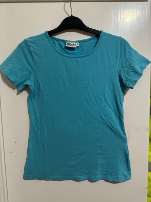 Turkos t-shirt från Tribute strl: M - Enkel turkos t-shirt från Tribute med rund halsringning och korta ärmar. Tillverkad i mjuk bomull, perfekt för en avslappnad stil. Passformen är normal och modellen är klassisk utan tryck eller detaljer.