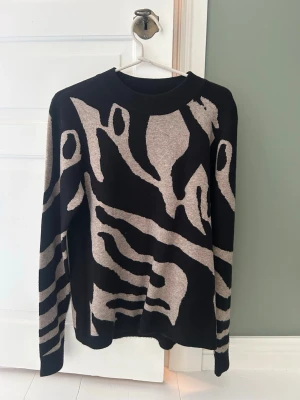 Svart och beige stickad tröja med liknade zebramönster  - Zebra liknande mönster. Använt en gång innan. Köpt hos ALMA men är från objekt. Köpte i storlek L just för att den inte skulle sitta tajt på mig men den har ett stretchigt material så passar dem flesta💕köpt för 500kr