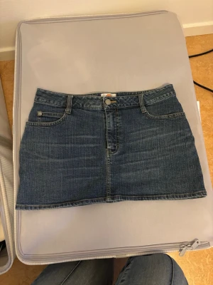 Blå jeanskjol med Tweety-broderi - Lågmidjad jeanskjol med klassiska fickor fram och bak. Köpt second hand i Köpenhamn, sparsamt använd. Tyvärr för liten för mig. Kjolen har ett broderat Tweety-motiv på ena bakfickan och stängs med knapp och dragkedja. 