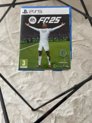 EA Sports FC 25 till PS5 - Säljer spelet EA Sports FC 25 till PlayStation 5. Omslaget är blått och spelet har fotbollstema med spelare i vita matchställ på framsidan. Perfekt för dig som gillar sportspel och vill spela med vänner eller online.