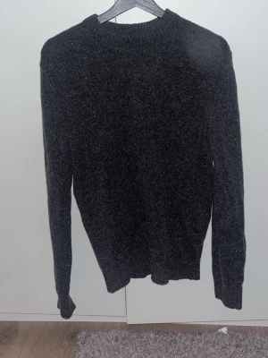 Mörkgrå stickad tröja Dressmann - Mörkgrå stickad tröja från Dressmann med rund halsringning och ribbade muddar vid ärmslut och nederkant. Klassisk och enkel design som passar perfekt till höst och vinter. Materialet känns mjukt och värmande.