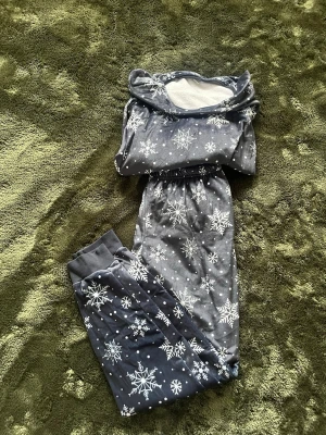 Mysig blå pyjamas med snöflingor - Blå pyjamas från Pepperts! med vita snöflingor som mönster. Setet består av långärmad tröja med mjuk, vit fleece på insidan och matchande byxor med muddar vid bensluten. Perfekt för kalla vinterkvällar och riktigt mysig känsla.💕